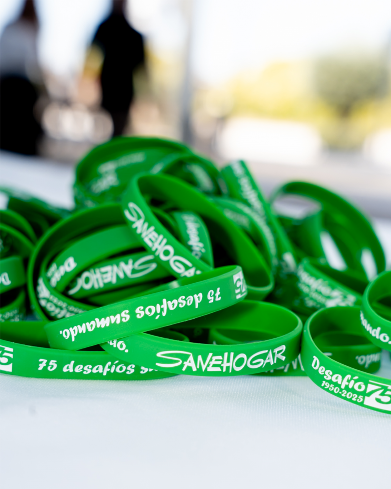 Pulseras verdes de Sanehogar con el mensaje 75 desafíos Sanehogar, apiladas sobre una mesa en un evento.